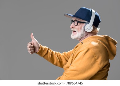 Side View Profile Of Content Old Man Having Fun With Earphones. Isolated On Grey Background