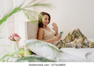 Side View Profile Cute Young Woman In Casual Casual Clothes Sit In Bed Hold In Hand Use Mobile Cell Phone Get Video Call Wave Hand Spend Time In Bedroom Lounge Home In Own Room House Wake Up Good Day