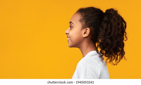 Side View Profile Portrait Of Cute African American Girl With Beaming Smile And Curly Hair In Ponytail Looking Aside At Empty Free Copy Space Isolated On Yellow Studio Background, Banner, Panorama