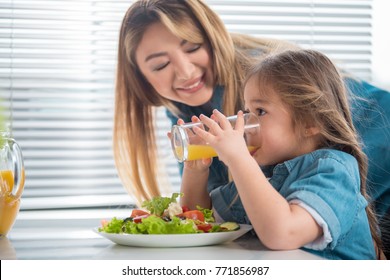 Side view profile of pretty little girl drinking orange juice with concentration. Her mom is looking at kid with love and smiling while standing in kitchen స్టాక్ ఫోటో