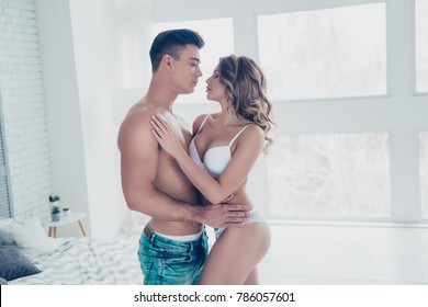 Side view profile of stunning, young macho with naked torso in jeans embracing with sexy woman with perfect buttoks, butt, curly hair, in white bikini, looking to each other, celebrate valentine day