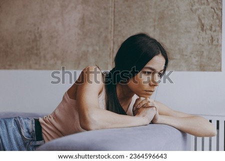 Side view profile worried frowning minded young latin woman 20s in casual clothes sit on sofa think plan hands folded under chin spend time in living room home in own house. People emotions concept