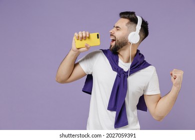 Side View Profile Young Brunet Man 20s Wears White T-shirt Purple Shirt Listen To Music In Headphones Keep Eyes Closed Sing In Mobile Cell Phone Isolated On Pastel Violet Background Studio Portrait.