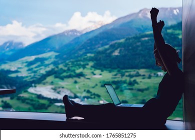 Side view of prosperous digital nomad celebrating lottery online win during networking time on modern laptop computer, happy excited female with raised hands reading good news about business triumph