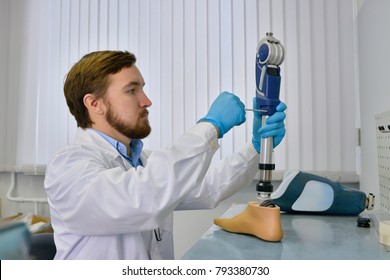 Side View Of  Prosthetics Technician Repairing Prosthetic Leg Part At Desk In Office, Checking It For Quality And Making Adjustments