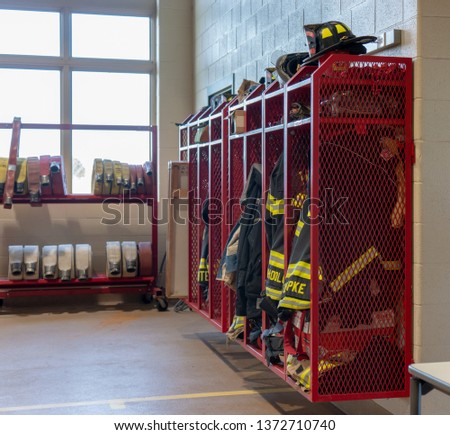 A side view of a rack of firefighters' gear and clothing in a firehouse. No personally identifiable names are shown. Concepts of emergency services, fire safety, and protection