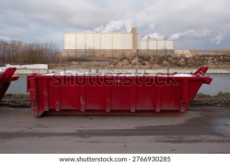 Side view of red skip container near water with industrial factory background