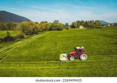 Side view of a red tractor mowing a grass field in the countryside on a sunny day - Shutterstock ID 2269499435