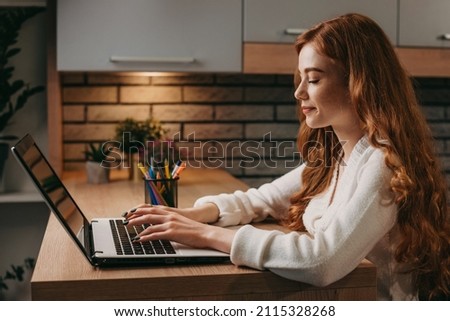 Side view of a red-haired businesswoman freelancer using the computer for distance work during the pandemic. Modern office interior. Internet technology. Online