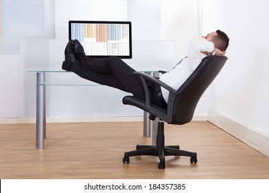 Side view of relaxed young businessman sitting feet up at office desk