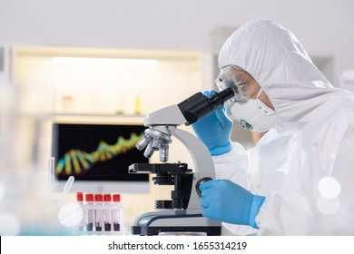 Side view of researcher in protective suit and mask using microscope while studying virus in laboratory