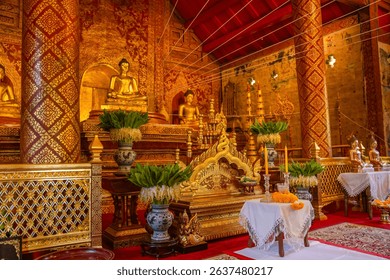 Side view of the richly adorned interior at Wat Phra Singh Woramahawihan, Chiang Mai, Thailand. The sacred hall showcases golden Buddha statues, traditional Lanna-style carvings.