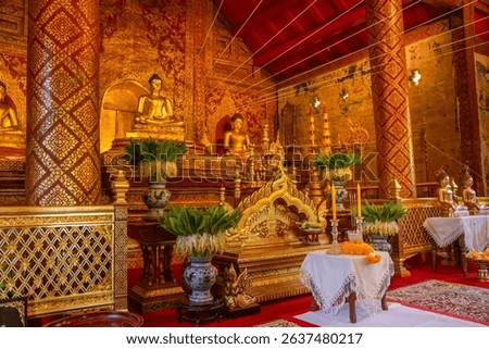 Side view of the richly adorned interior at Wat Phra Singh Woramahawihan, Chiang Mai, Thailand. The sacred hall showcases golden Buddha statues, traditional Lanna-style carvings.