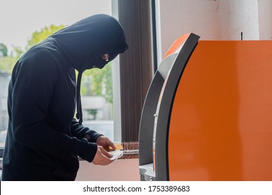 Side View Of Robber In Mask Holding Credit Cards Near Automated Teller Machine