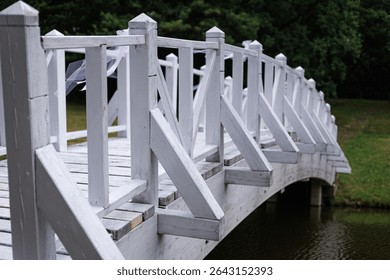 Side view of rustic white bridge over calm water in green park. Concept: vintage charm, outdoor event, peaceful vibe.