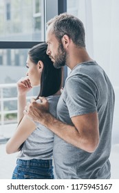 Side View Of Sad Couple Standing Together And Looking At Window