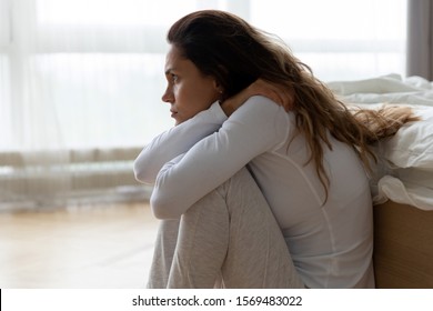 Side View Sad Pensive Woman In Night Clothes Sit On Floor Hugs Knees Leaned On Bed Feels Lonely, Hard Get Over Separation With Boyfriend, Chronic Insomnia Caused By Anxiety, Stress, Depression Concept