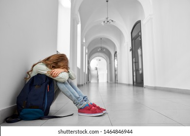 Side view of sad school girl sitting on floor at corridor and hiding face by hands and crying. Blonde girl having bad mark and terrible mood after lessons. Concept of hard period of teenagers. - Powered by Shutterstock