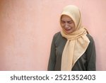 Side View Of Sad Young Asian Muslim Woman Wearing Hijab Looking Down And Crying, Standing Against Pink Background