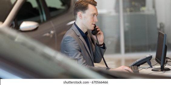 Side View Of Salesman Talking On Landline Phone In Car Showroom