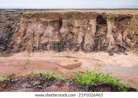 Side view of the sandstone soil layer under the asphalt road, which was eroded by rain and wild water flows, eroded and damaged, common in the Thai countryside during the renovation period.