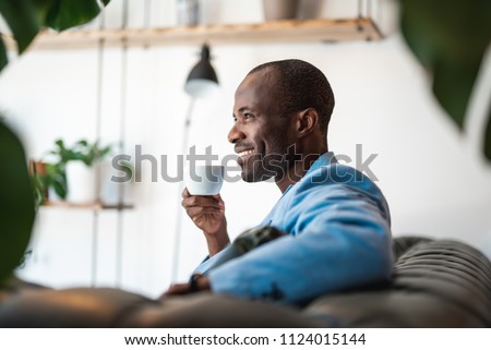 Side view satisfied man drinking mug of delicious beverage while relaxing on cozy sofa during break