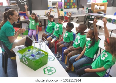 Side view of school kids wearing recycle tee-shirt raising hand to answer at a question asking by their teacher sitting in front of them - Powered by Shutterstock