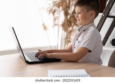 Side View Of A Schoolboy At Home Schooled Working On A Laptop Typing Text On The Keyboard While Communicating With A Remote Teacher. The Child Is Studying Computer Programs Online. Education Concept.