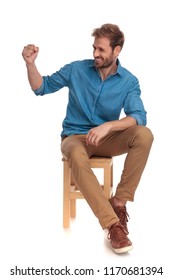 Side View Of A Seated Casual Man Laughing With Fist Up In The Air On White Background