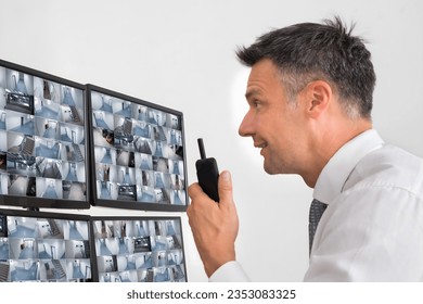 Side view of security system operator using walkie-talkie while looking at CCTV footage