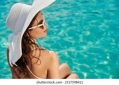 Side view of seductive girl sunbathing, sitting near swimming pool. Brunette young female looking up, relaxing, enjoying vacation. Concept of summertime, leisure and activity.