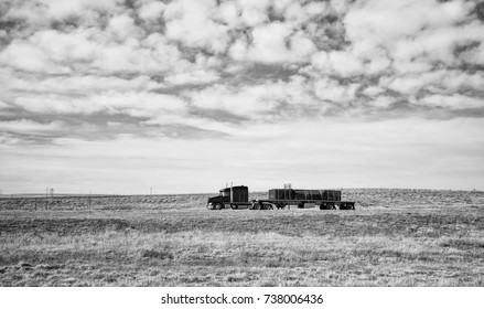 Side View Of A Semi Truck Hauling Freight On A Flatbed Driving Down Interstate In A Black And White Wyoming Countryside Landscape