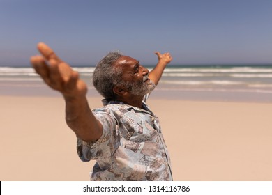 Side View Of Senior African American Man With Arms Outstretched Standing On Beach In The Sunshine