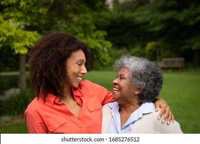 Seitenansicht der älteren Afroamerikanerin mit ihrer Tochter im Garten, lächelt einander an und umarmt. Familie genießt Zeit zu Hause, Lifestyle-Konzept