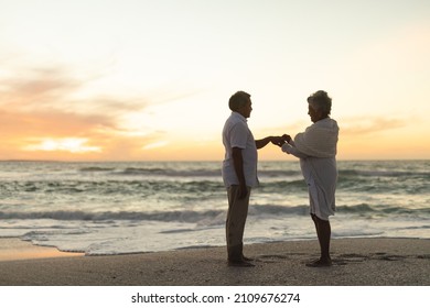 Side view of senior biracial bride putting wedding ring on groom's finger at beach during sunset. lifestyle, love and culture. - Powered by Shutterstock