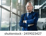 Side view of senior businessman ceo standing in office lobby arms crossed. Mature business man wearing blue suit formal wear looking away through window.