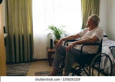 Side view of senior Caucasian male patient  looking outside the window while sitting in wheelchair in bedroom at retirement home,Social distancing and self isolation in quarantine lockdown for Covid19 - Powered by Shutterstock