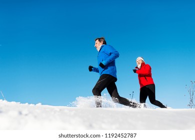 A Side View Of Senior Couple Jogging In Snowy Winter Nature.