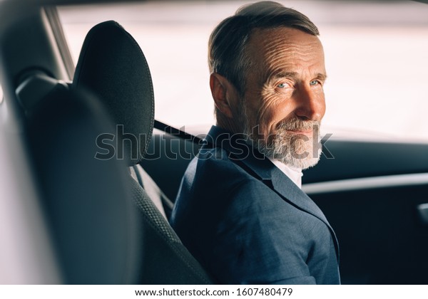 Side view of a senior driver looking away.\
Man in formal wear sitting inside a\
car.