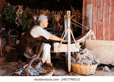 Side view of senior female in casual farm clothes sitting with baskets of fresh wool and while working and threshing wool using a carding machine in local cloth making shop - Powered by Shutterstock