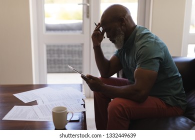 Side view of senior man filling form while using digital tablet in living room at home - Powered by Shutterstock