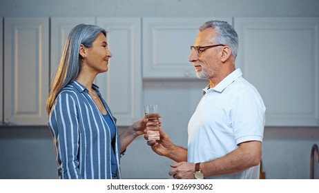 side view of senior man giving glass of water to happy asian wife
