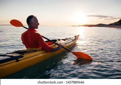 Side View Of Senior Man Paddling Kayak On The Sunset Sea