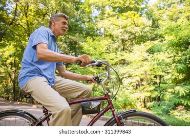 Side view of senior man is riding bicycle in park.