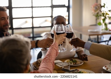 Side view of senior multi-ethnic group at cookery class, sitting at a table relaxing together, holding glasses of red wine and making a toast. Active Seniors enjoying their retirement. - Powered by Shutterstock