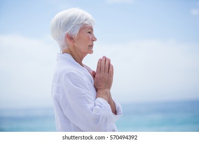 Side view of senior woman with hands clasped at beach against sky - Powered by Shutterstock