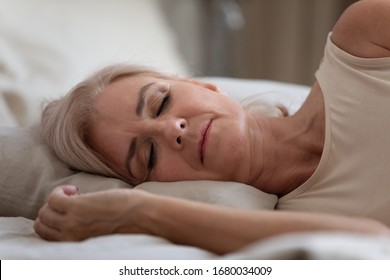 Side View Serene Older Woman Sleeping On Comfortable Pillow In Bedroom. Head Shot Close Up Peaceful Middle Aged Female Retiree Enjoying Sweet Dreams At Home, Resting Alone At Night Or Weekend Morning.