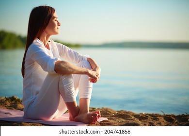 Side view of serene woman sitting on sandy beach against blue sky outdoors - Powered by Shutterstock