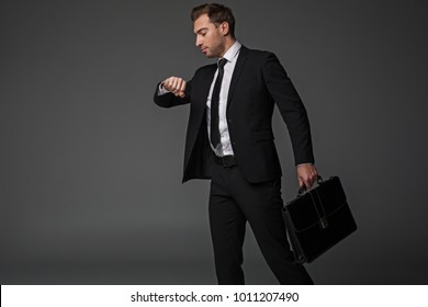 Side view serene worker looking at watch while going at job. He keeping suitcase in arm. Profession concept. Isolated and copy space