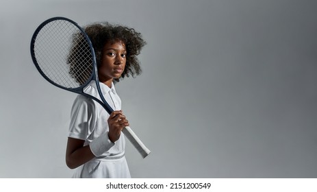 Side view of serious african girl tennis player with racket looking at camera. Curly female child wear sportswear. Healthy and sports lifestyle. Isolated on white background. Studio shoot. Copy space - Powered by Shutterstock